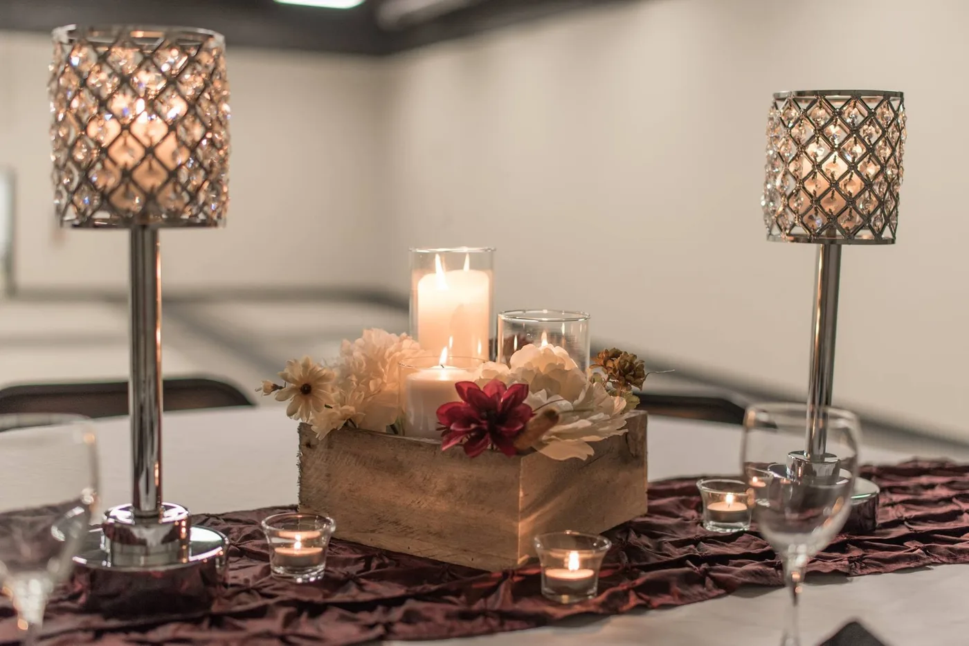 A table centerpiece with crystal candle lamps, candles, and florals on a burgundy runner